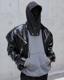 Person wearing a black glossy jacket over a gray hoodie against a concrete wall.