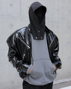 Person wearing a black glossy jacket over a gray hoodie against a concrete wall.