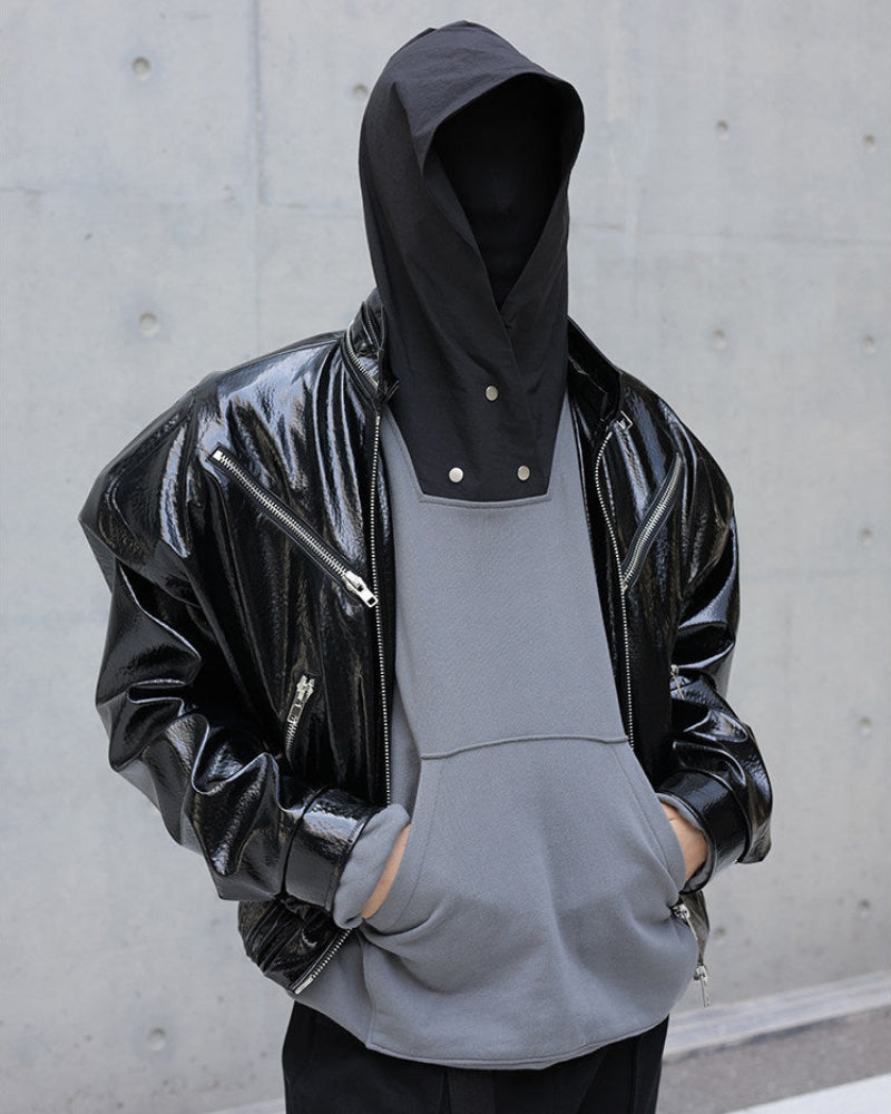 Person wearing a black glossy jacket over a gray hoodie against a concrete wall.