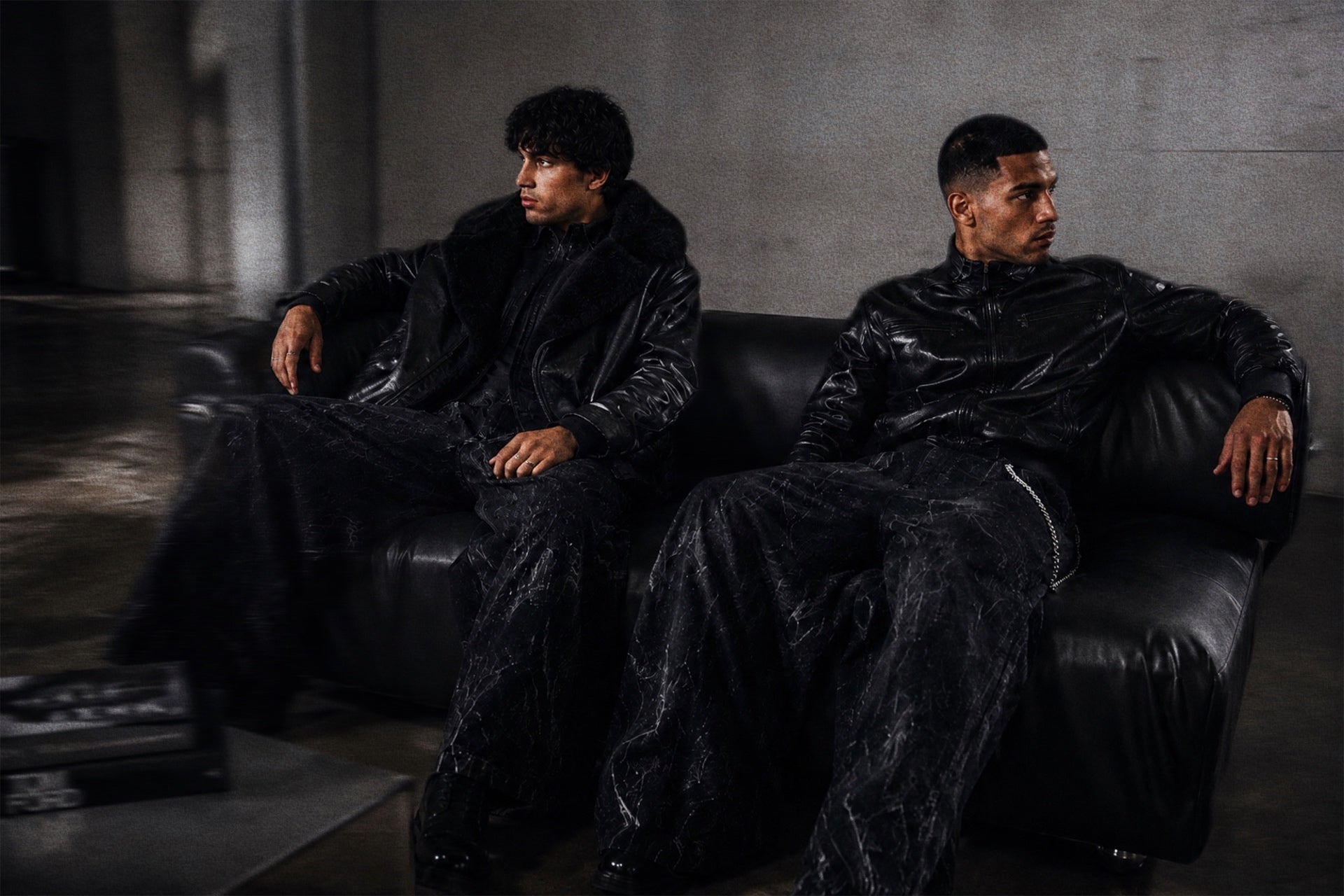Two men in black velvet outfits sitting on a dark couch in a dimly lit room with OFFCULTURE STREETWEAR AND DARKWEAR OUTFIT